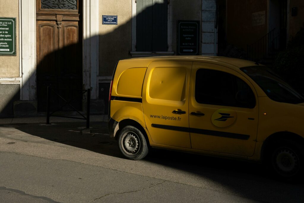 A yellow postal van parked on a sunny street in Provence, France.