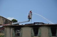Firefighter sprays water from ladder truck to extinguish roof fire on building.
