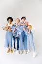 Full length of multiracial friends in casual clothes standing in studio while holding child on hands on white background while looking at camera