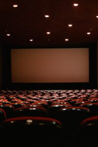 A dimly lit empty cinema theater with rows of red chairs facing a projector screen.