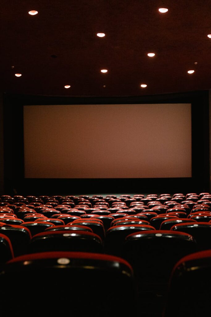 A dimly lit empty cinema theater with rows of red chairs facing a projector screen.